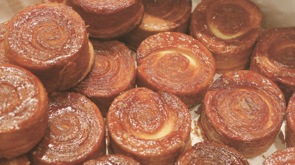 : Zoom sur plusieurs petits kouign-amann dorés et caramélisés, aux contours croustillants et au cœur fondant, alignés sur une plaque de pâtisserie artisanale.