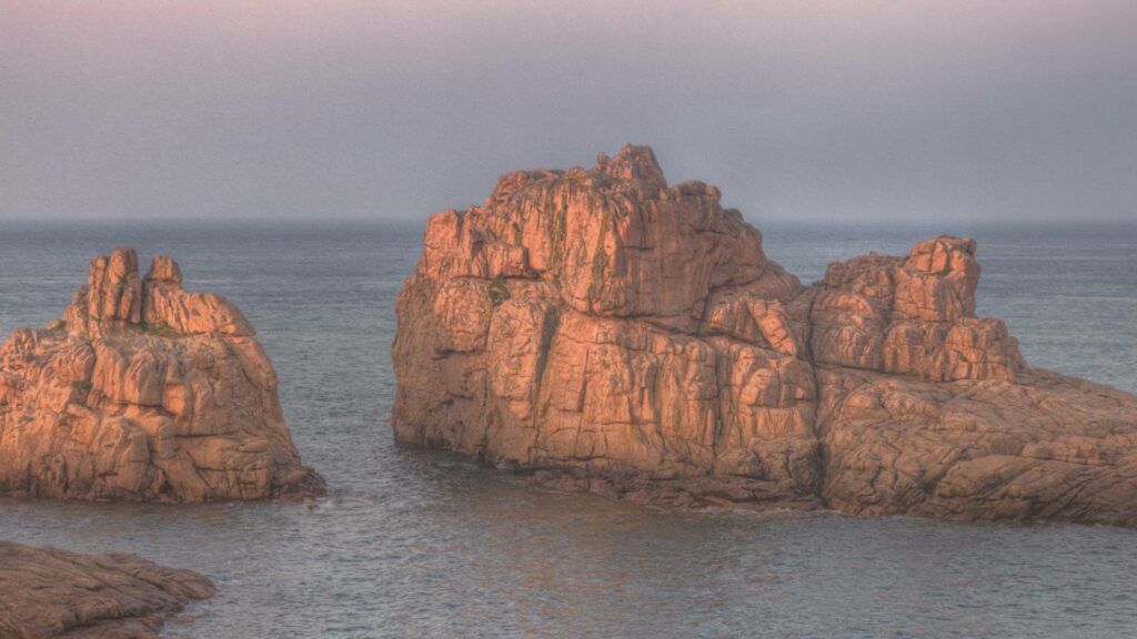 Rochers rosés de Ploumanac’h baignés de lumière dorée au crépuscule, entre ciel pastel et mer d’huile.