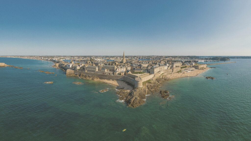Remparts de Saint-Malo surplombant la mer à marée haute, baignés d’une lumière estivale douce.
