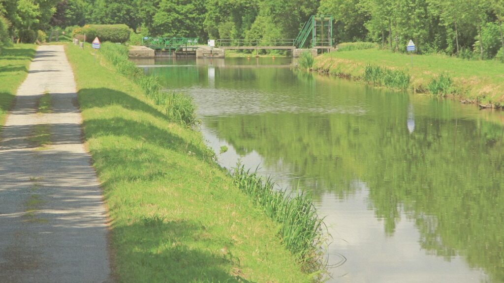 Vue paisible du canal de Nantes à Brest serpentant entre les arbres, reflet du ciel d’été sur l’eau calme et sentier de halage bordé de verdure.