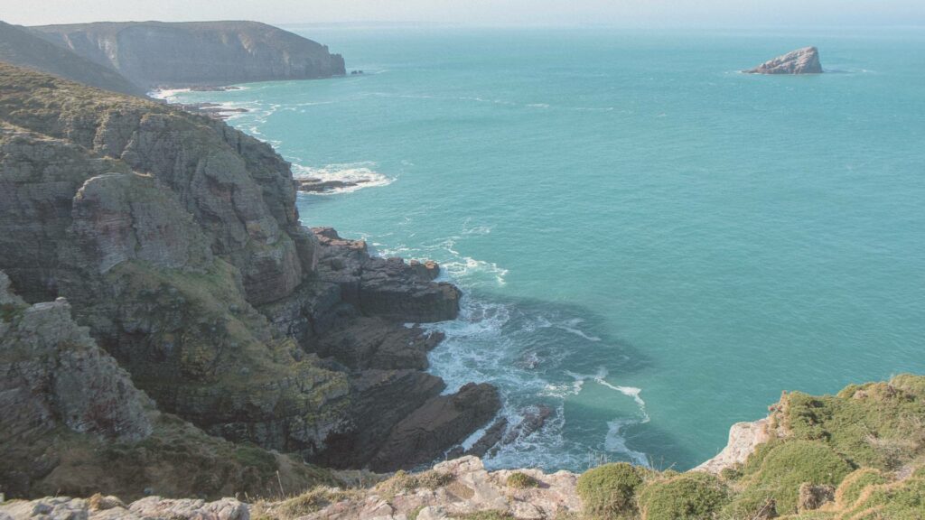 Panorama du Cap Fréhel avec falaises escarpées et végétation sauvage sur fond d’océan turquoise.