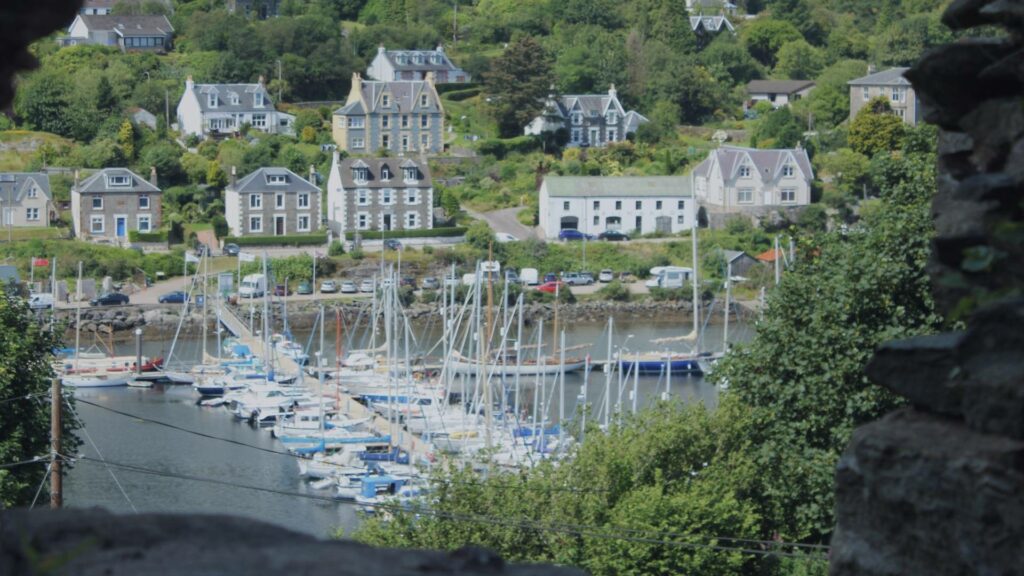 Vue sur le port de Tarbert avec ses maisons colorées, ses bateaux de pêche et les collines verdoyantes en arrière-plan sous un ciel changeant typiquement écossais.