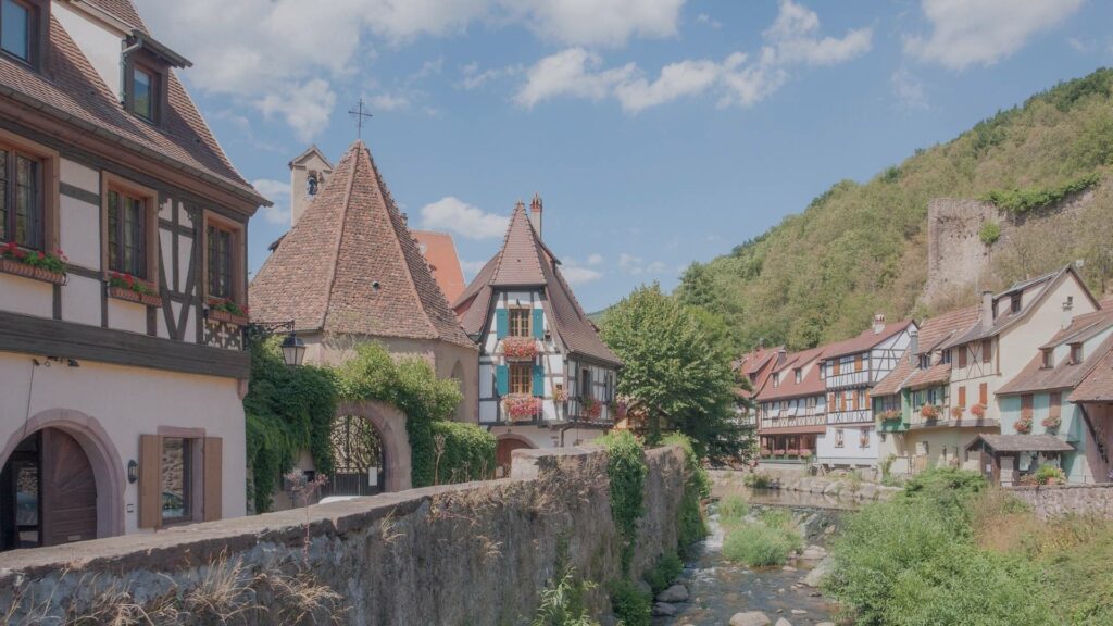 Vue panoramique de Kaysersberg en hiver, avec ses maisons à colombages enneigées, la rivière Weiss et les collines d’Alsace en arrière-plan