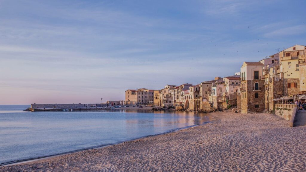 Vue sur Cefalù avec sa cathédrale normande, ses maisons serrées en bord de mer, les eaux turquoise de la Méditerranée et le rocher de la Rocca en arrière-plan.