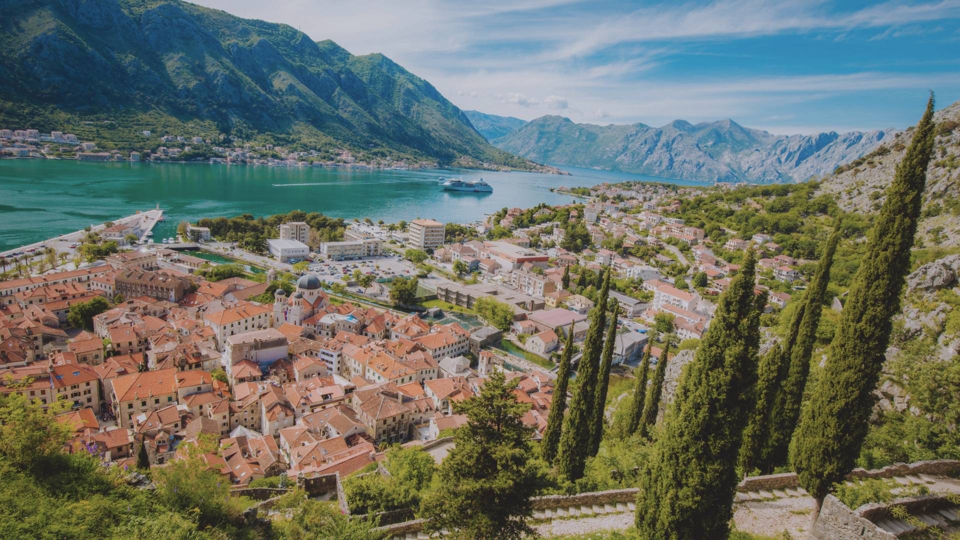 Vue aérienne sur Kotor, ses toits rouges depuis la forteresse perchée sur la montagne et les eaux turquoise de la baie encerclées par les reliefs.