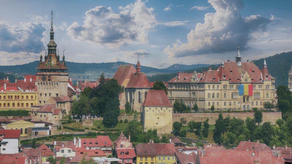 Vue colorée sur les toits rouges et les maisons pastel de Sighișoara, dominées par la Tour de l’Horloge, sous un ciel clair de début de printemps.