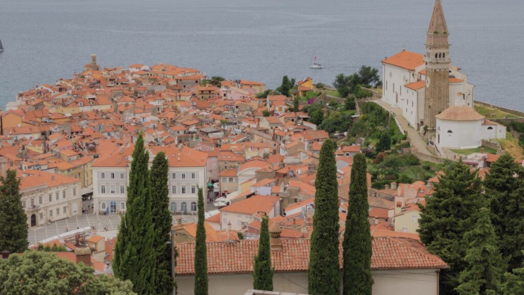 Vue sur Piran depuis les remparts, avec les toits rouges, la place Tartini, la mer Adriatique et l’église Saint-Georges sur les hauteurs, sous un ciel clair de mai.