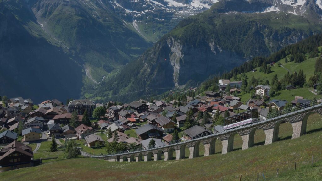 Vue sur le village de Mürren entouré de chalets fleuris, dominant la vallée de Lauterbrunnen avec les sommets enneigés de l’Eiger, Mönch et Jungfrau en toile de fond.