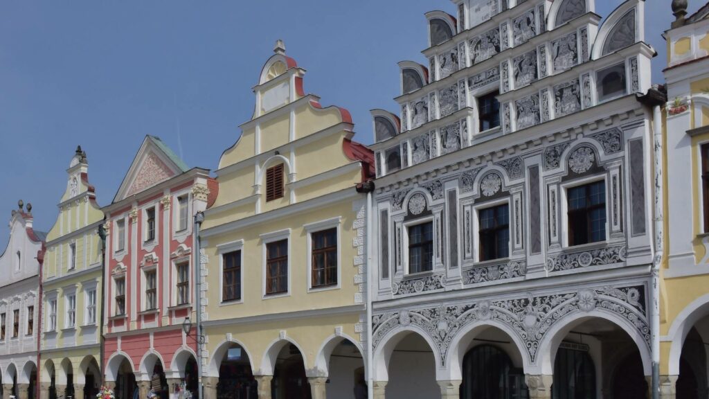 Vue sur la place principale de Telč, avec ses maisons colorées de style Renaissance, ses arcades et son sol pavé, sous un ciel lumineux de printemps.