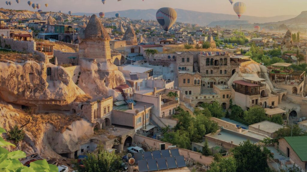 Vue aérienne de Göreme au lever du soleil avec des montgolfières colorées flottant au-dessus des cheminées de fées et des habitations troglodytiques.