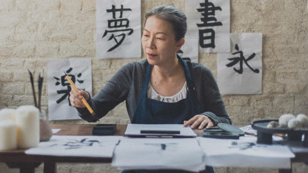 Femme japonaise assise à une table, concentrée sur la calligraphie d’idéogrammes – une scène empreinte de calme et de précision, symbole de l’ikigai dans l’attention portée à chaque geste.